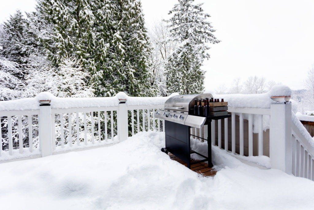 BBQ cooker with bottles of beer during winter time on home outdoor deck