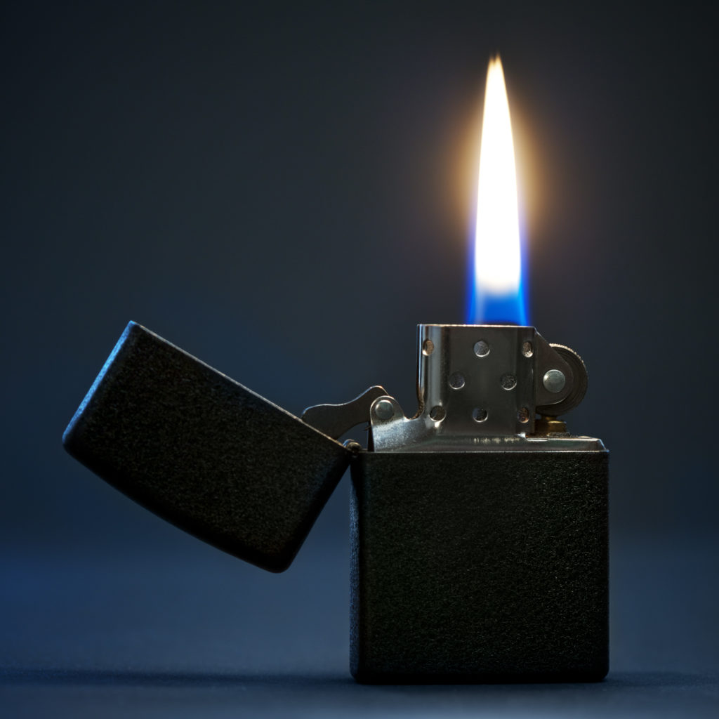 black gasoline lighter with flame on dark background