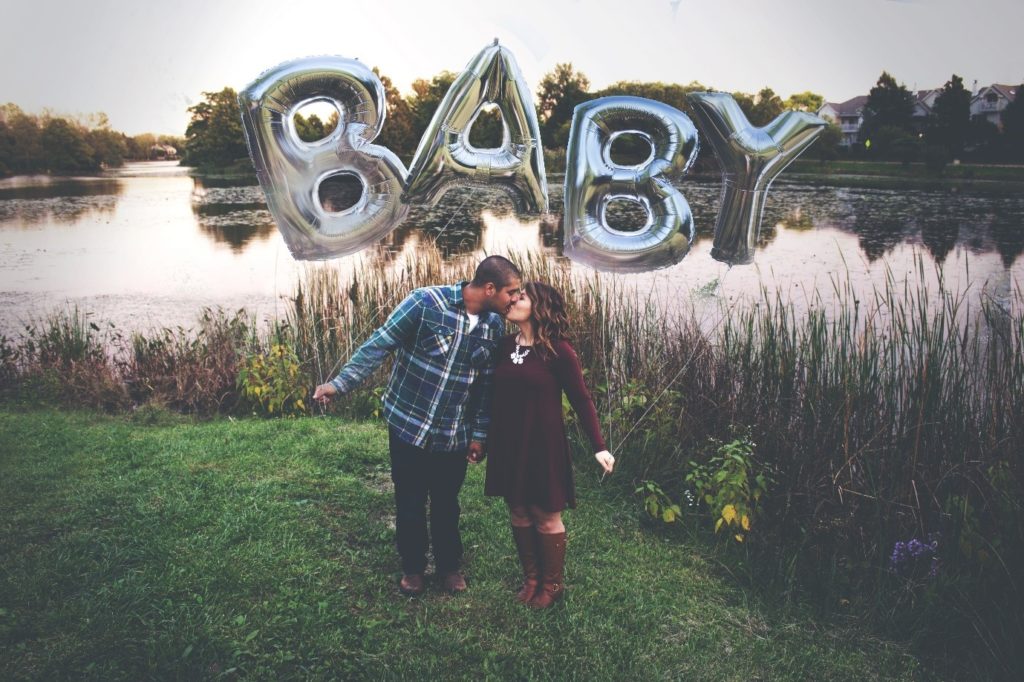 Couple in a field stood with a large foil and plastic helium filled balloon spelling baby