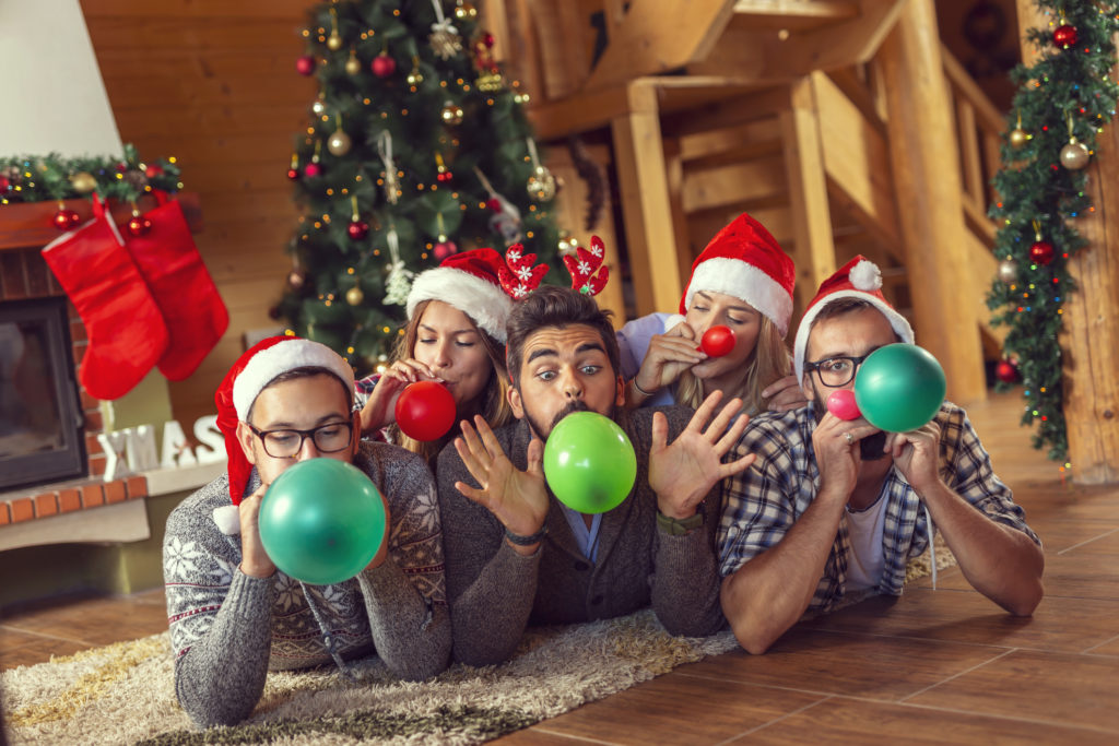 Group of friends lying next to a fireplace and Christmas tree, having fun on Christmas morning, blowing colorful balloons and decorating the house