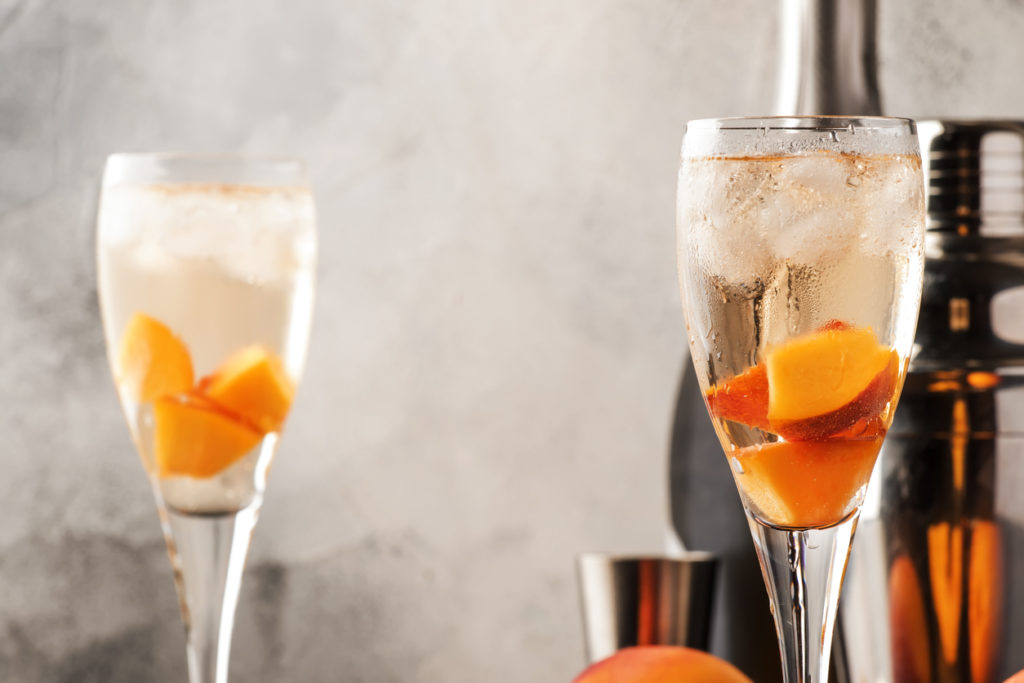 Bellini, alcoholic cocktail with sparkling wine, sugar syrup, lemon juice, peach and ice, gray table background, copy space