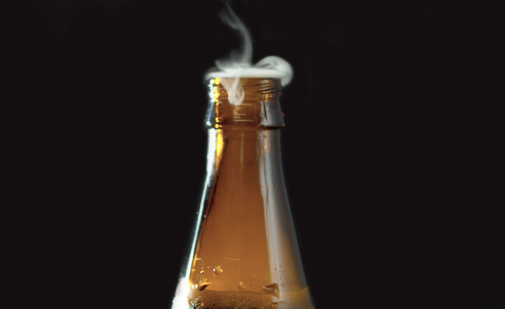 Close up open bottle of beer on black background. Foam and bubbles begin to rise in the bottle and gas escapes from the neck.