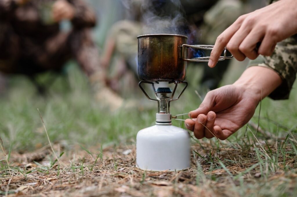 Outside in nature, a camping stove with a metal pot over the top, cooking food