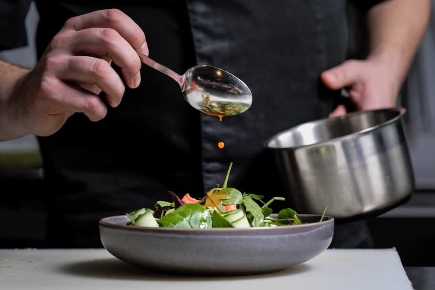 A person pouring sauce into a bowl of salad