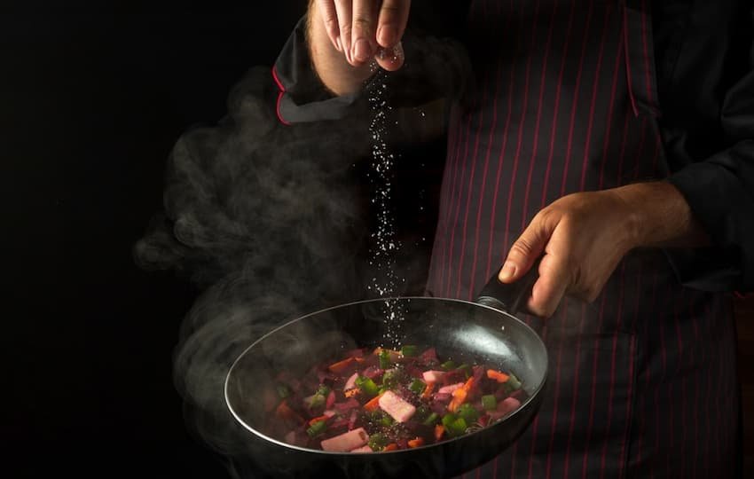 A person pouring salt into a pan of food