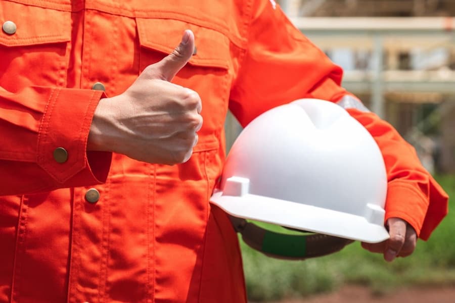 A person in an orange jumpsuit holding a white hard hat