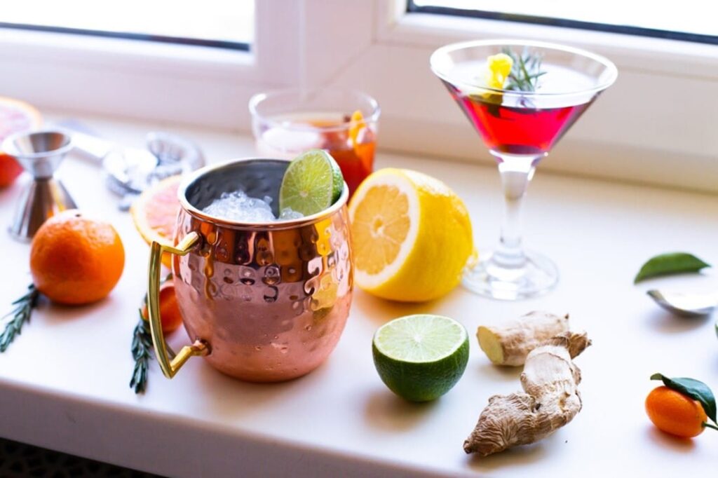 A copper mug with ice and lemons next to a glass of liquid