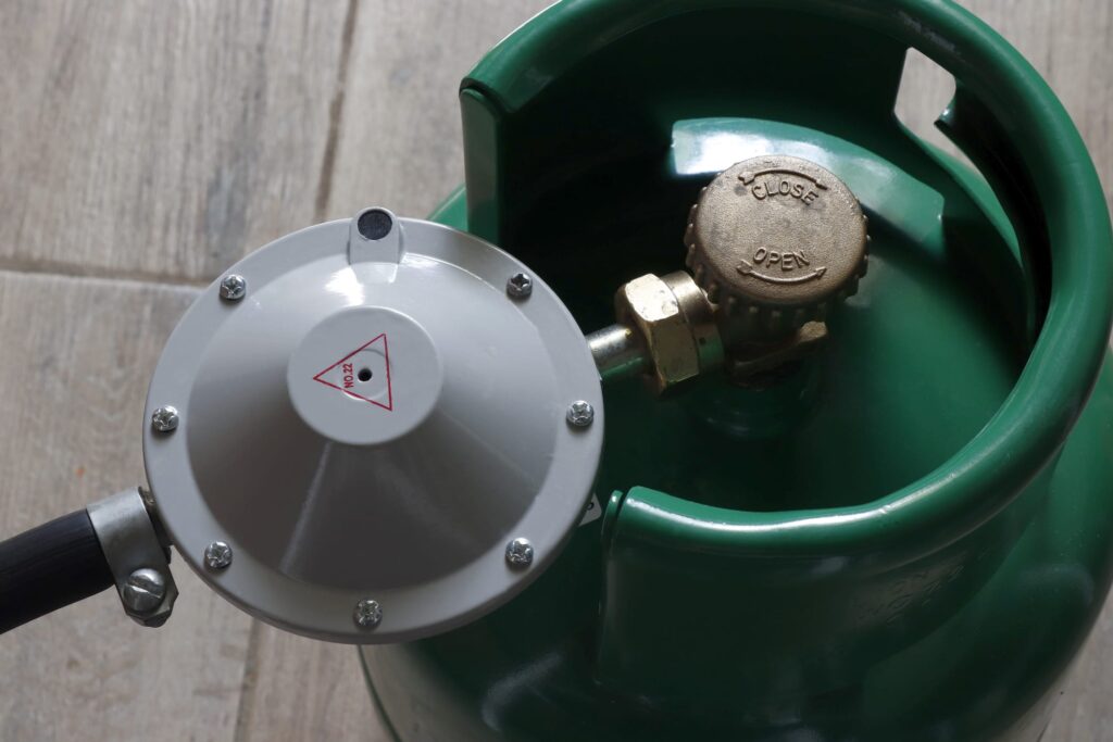 Image of a household gas cylinder of a small volume in green with a connected hose and reducer.